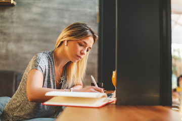 Young woman writing a note with pen with laptop on table at a coffee shop.