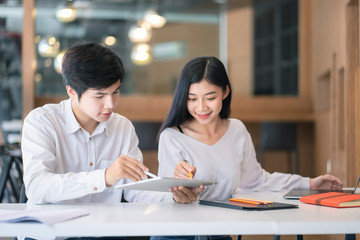 Young Asian couple or college student using digital tablet and laptop computer notebook work together at coffee shop or university campus.
