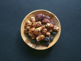 Dates in a wooden bowl on a black background.