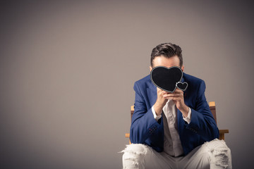 Shy man hiding behind heart shaped chalkboard.