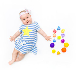 Portrait of a sweet infant baby girl wearing a pink dress and headband bow, isolated on white in studio with number seven from toys