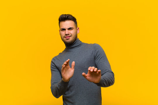 Young Hispanic Man Feeling Disgusted And Nauseous, Backing Away From Something Nasty, Smelly Or Stinky, Saying Yuck Against Orange Wall