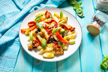 Pasta with grilled vegetables - zucchini, eggplant, pepper ant tomato on wooden background.