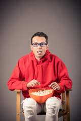 Nerdy man eating popcorn against the wall.