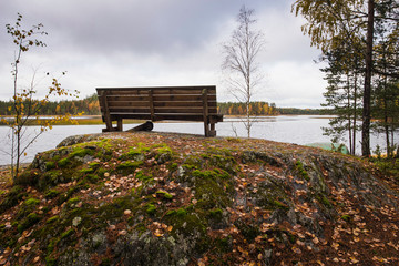 Rock with wooden bench by lake in autumn