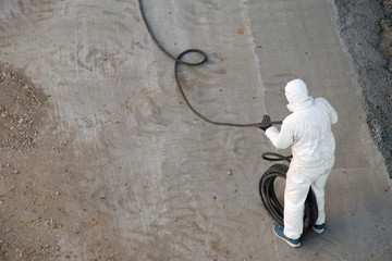 Construction worker in white protective  jumpin suit wrapping a long hose