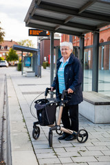Very old senior woman waiting at the bus stop with walker