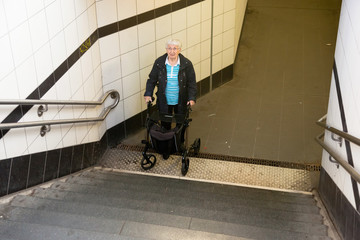 Very old senior woman with walker can not walk up the stairs in a train station