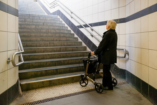 Very old senior woman with walker can not walk up the stairs in a train station