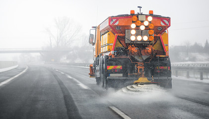 Snow plow salting street in winter time. Orange truck deicing. Maintenance winter vehicle back side. - Powered by Adobe