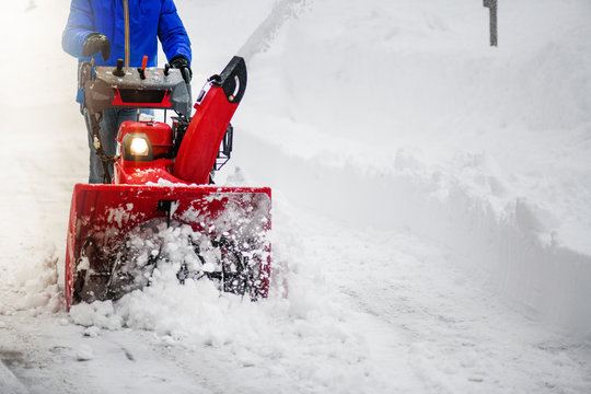 Man clearing or removing snow with a snowblower on a snowy road detail.