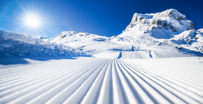 New groomed ski piste or slope. Lines in snow with sunny mountains background. Winter skis concept.