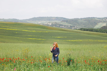Fototapeta na wymiar Young woman smelling red flower in the field in Tuscany, Italy