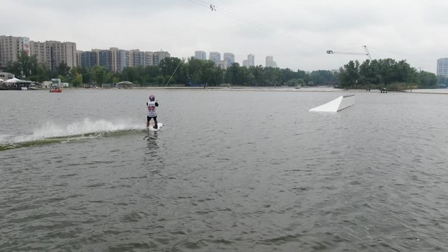Wakeboarder is sliding on a rail then jumping on the water, cloudy day