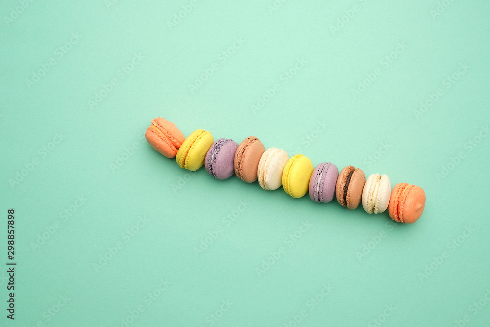 Poster round multi-colored baked macarons with cream lie in a line on a green background