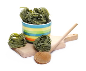 Raw tagliatelle green spinach pasta with spoon in colorful porcelain bowl on wooden chopping board...