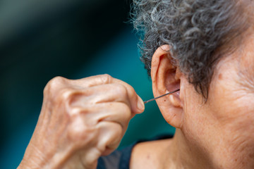 Senior woman putting ear pick into her right ear, Grey curly hairs, Swimming pool background, Close up & Macro shot, Selective focus, Asian Body part, Healthcare concept, Symptom of hearing loss