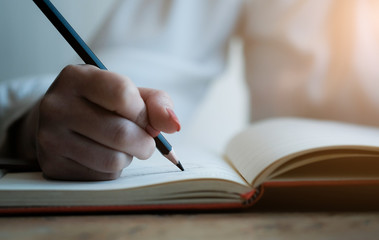 Woman hand with pencil writing on notebook. making notes in notebook with pencil. People writing on notebook and work on wooden table