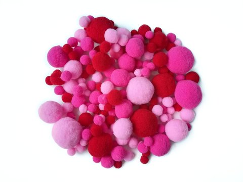 Variety size pom pom made from pink and red fiber yarn arranged circle on white background