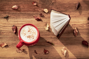 Coffee cup and open book on wooden table with autumn leaves. Top view. Concept of romantic mood, back to school, education