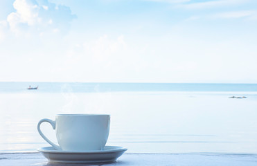 Hot coffee in a white cup with saucer on a wooden table Background blurry boat and sea.