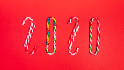 Festive creative christmas banner of numbers 2020 of multicolored traditional xmas candy canes on red background.