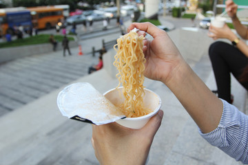 Young woman hand holding plastic fork of instant noodles, Sodium diet high risk kidney failure,...