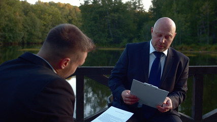 People in suits sit at a table and discuss documents.