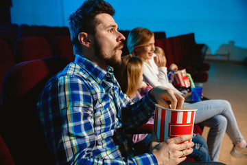 Young caucasian family watching a film at a movie theater, house or cinema. Look expressive, astonished and emotional. Sitting alone and having fun. Relation, love, family, childhood, weekend time.