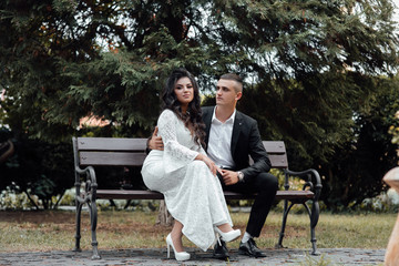 Couple of love sitting on bench. Handsome man and attractive young woman are in love. Romantic couple in summer day. Fashionable photo of young couple. Couple in love - beginning of a love story.