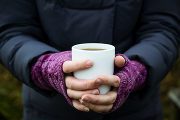 White Cup with tea in hand. Knitted purple fingerless gloves on the hands of a woman on the street.