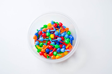 Small multi-colored plastic parts of children's mosaic in a transparent round container on a white background.