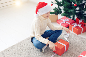 Holidays, christmas, childhood and people concept - smiling happy teen boy in santa hat opens gift box over christmas tree background