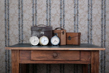 3 vintage alarm clocks on an old wooden table in front of an old  textured carpet
