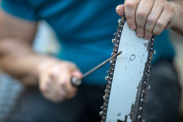 Sharpening a chainsaw Close up on a man sharpening a chainsaw chain with file