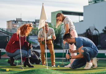 Group of smiling friends enjoying together playing mini golf in the city. - obrazy, fototapety, plakaty