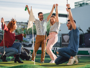Group of smiling friends enjoying together playing mini golf in the city.