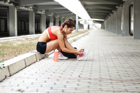 Young woman sitting at the city street and preparing for workout.