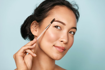 Beauty. Smiling woman brushing eyebrows with makeup brush closeup. Portrait of beautiful happy...