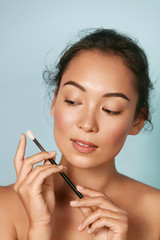 Fototapeta premium Beauty. Woman with perfect face skin holding makeup brush closeup portrait. Beautiful female model with flawless hydrated dewy facial skin and cosmetic brush at studio