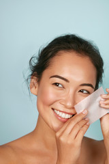 Face skin care. Smiling woman using facial oil blotting paper portrait. Closeup of beautiful happy...