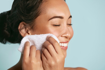 Woman cleaning facial skin with towel after washing face portrait. Beautiful happy smiling young asian female model wiping facial skin with soft towel, removing makeup. High quality studio shot