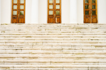 a wide white stone staircase leads to the entrance of a white building with columns and wooden doors