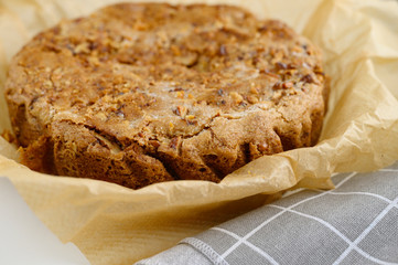a baked pie with a sprinkle of walnuts on baking paper, next to a grey checked towel, are arranged on a white background