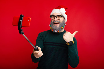 Photo of cheerful man with decorated beard taking selfie and showing thumbs up