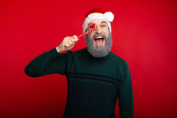 Fototapeta na wymiar Cheerful hipster man with white beard holding red xmas candy