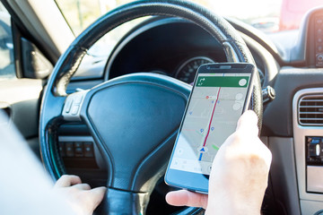 Closeup view of male hands with a mobile phone with map on screen while driving a car. Using the...