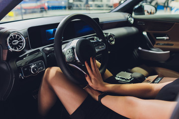 Long female legs on a steering wheel of a car.