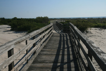 weathered wooden boardwalk with railing through beach dune