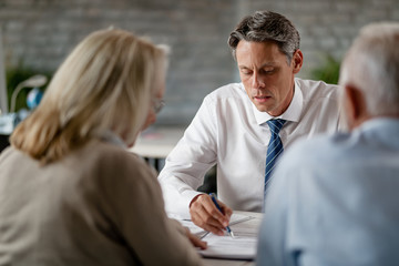 Financial advisor writing notes while having consultations with senior clients.